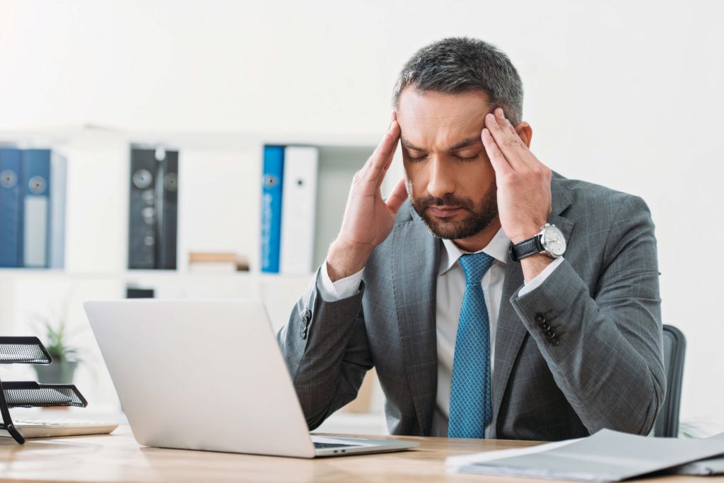 business man sitting at a desk and appearing to develop a headache thanks to what's on the laptop, medical billing